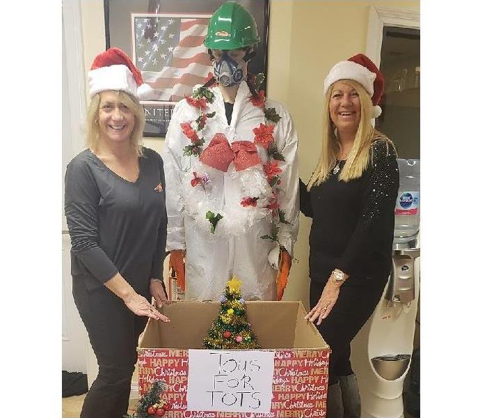 Two female SERVPRO associates beside 'Toys for Tots' collection box