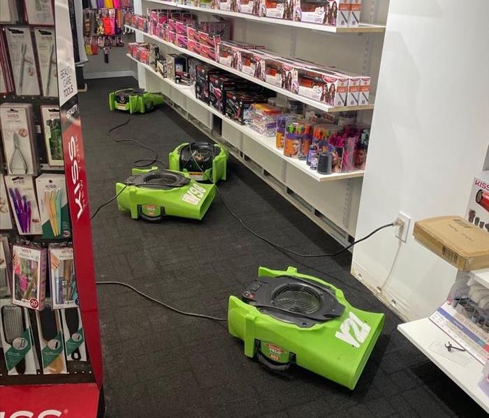 SERVPRO air movers on the carpet near store inventory shelves with removed baseboards and drywall