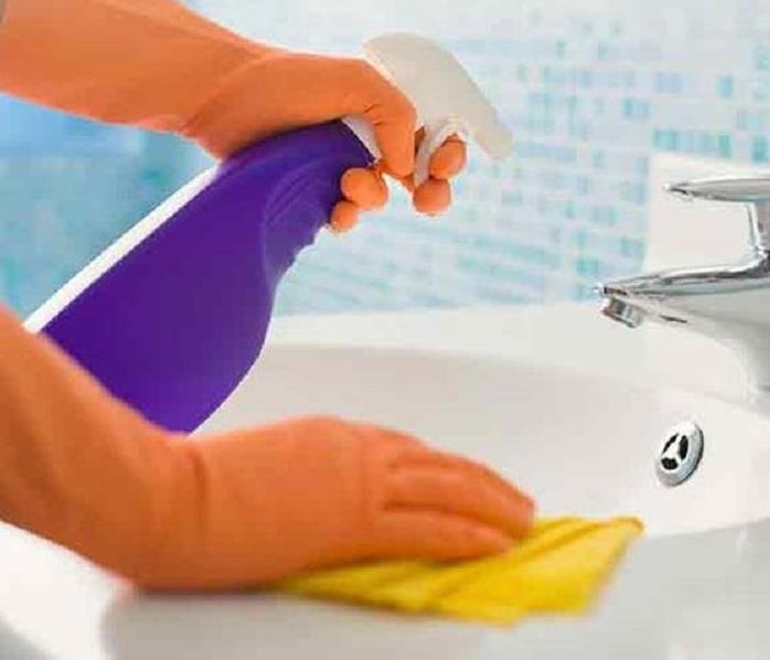 Gloved hands holding cleaning products and a cloth while cleaning a sink to make it sanitary