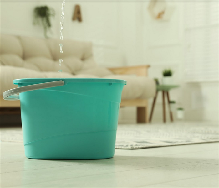 a bucket in a living room that is catching water falling from the ceiling